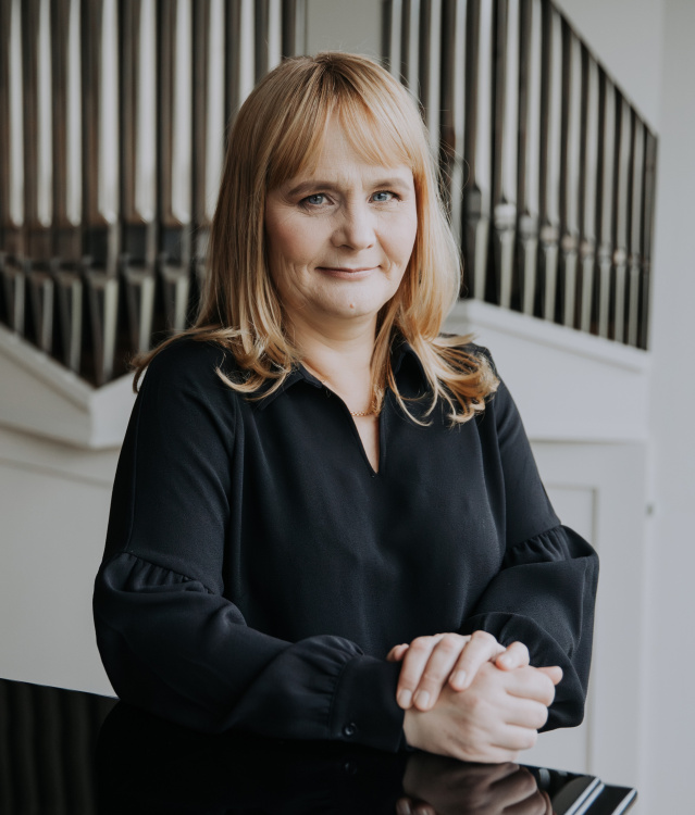 Urkukonsertti. Kristel Aer (Viro) Vaaleantukkainen nainen mustassa paidassa nojaa flyygeliin, taustalla urkujen julkisivu.