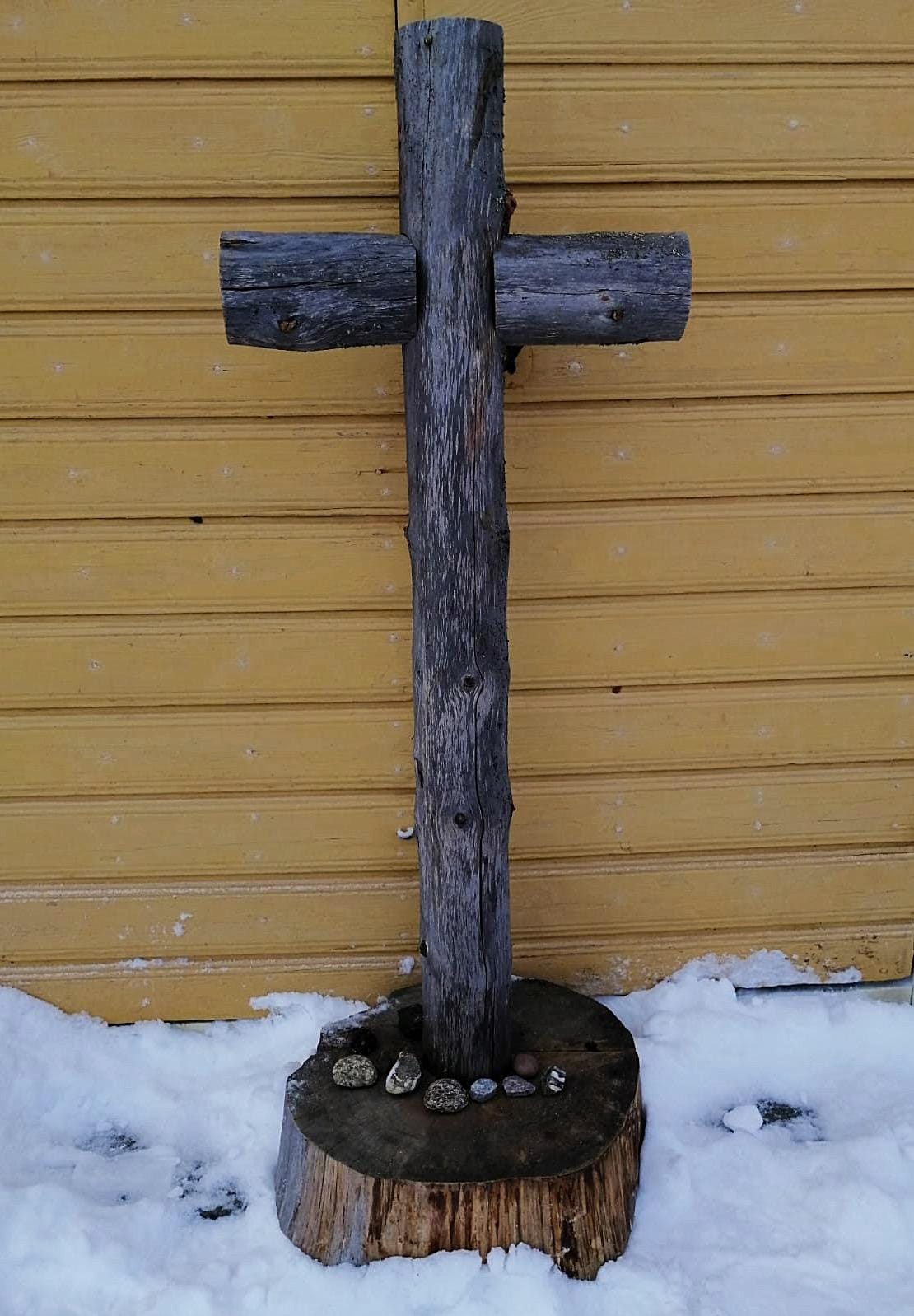 Pyhiinvaellusmessu Iso, puusta rakennettu risti vanhan talvihaudan keltaisen puuoven edustalla.